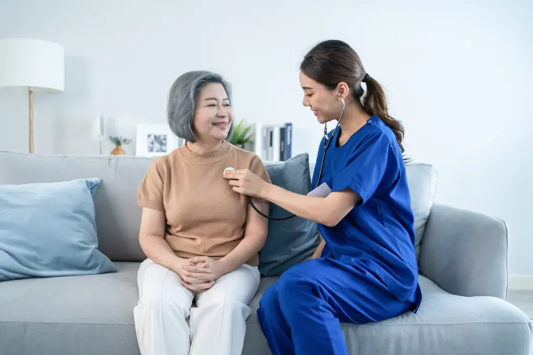 Woman nurse checking an elderly woman's heartbeat at an in-home primary care visit.