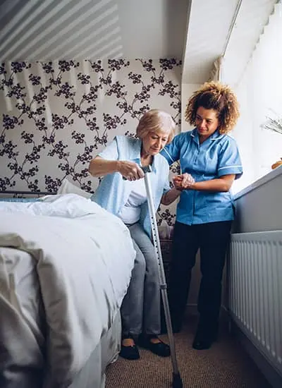 Nurse helping older lady out of bed at her home