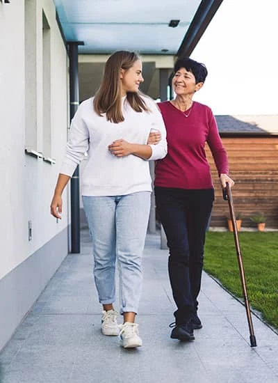 Comfort care volunteer helping lady with cane walking outside