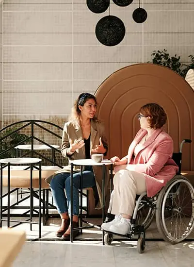 Two women one in a wheel chair sitting in a cafe discussing home health care services